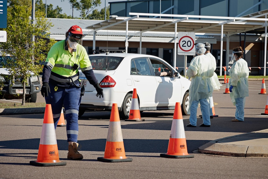 A car pulls up at a testing site. People at the site are in full PPE.