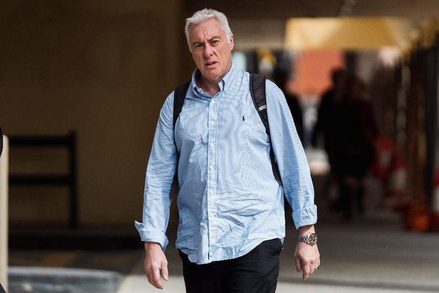 Paul Lawrence wearing a light blue business shirt walking on the footpath outside court.