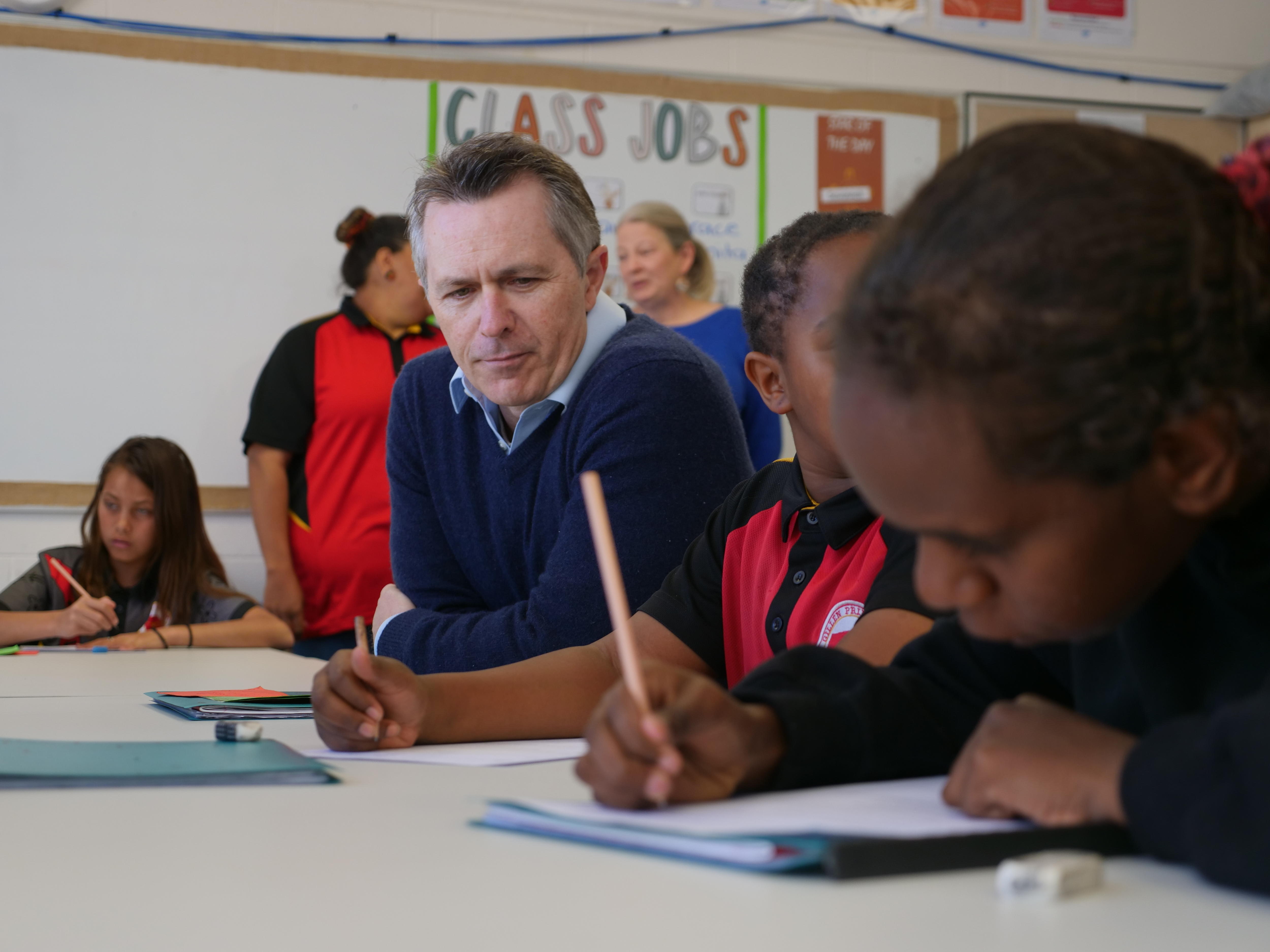 Jason Clare sits next to two students who are doing worksheets