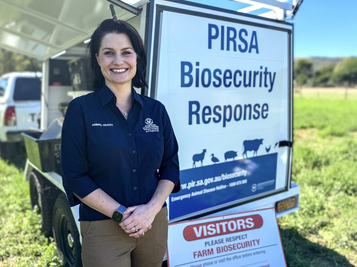 A woman in a blue shirt stands in front of a biosecurity response sign. 