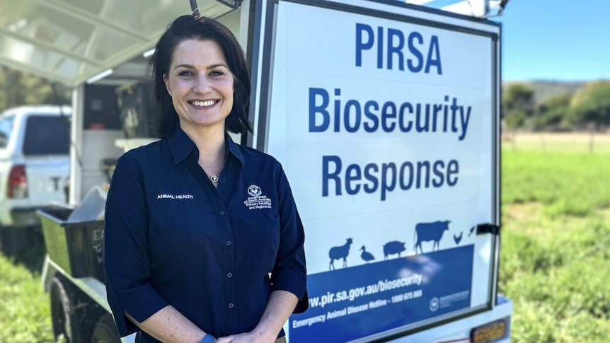 A woman in a blue shirt stands in front of a biosecurity response sign. 
