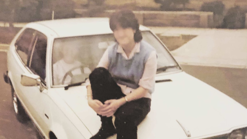 A young woman sits on the bonnet of a car.