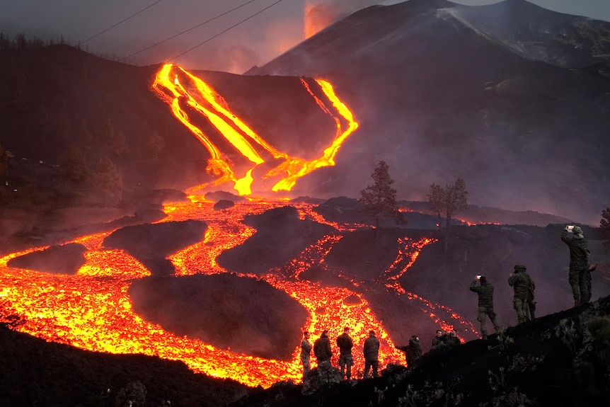 Ле-Расплавленный Лау, вытекающий из вулкана, и люди, наблюдающие за происходящим в сторонке