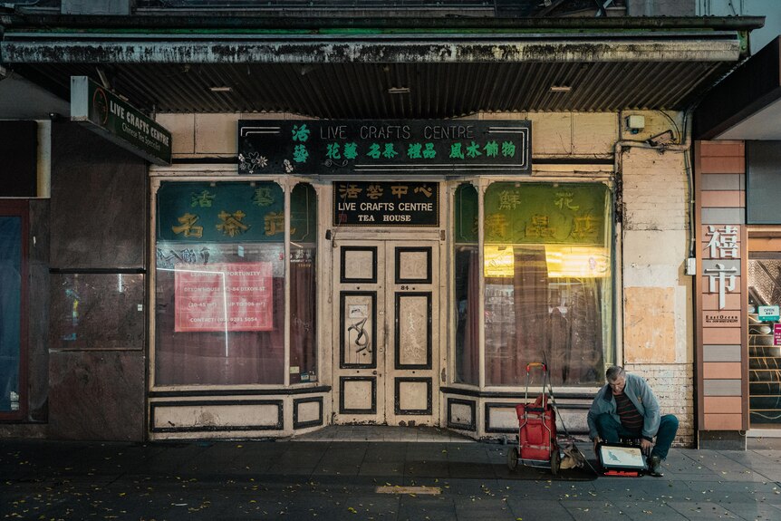 A photo of a man sitting in front of a closed shop in Sydney's Chinatown.