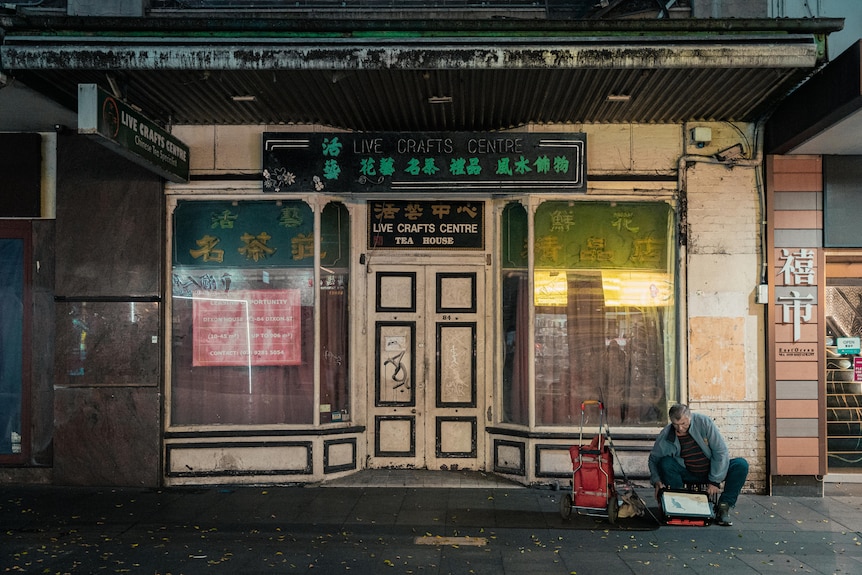 A photo of a man sitting in front of a closed shop in Sydney's Chinatown.