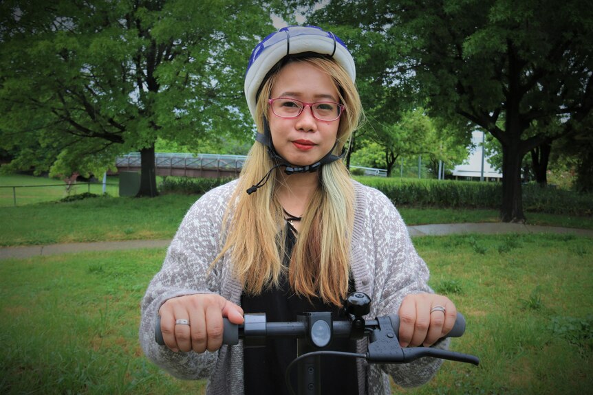 A woman with a helmet on a scooter looks at the camera.