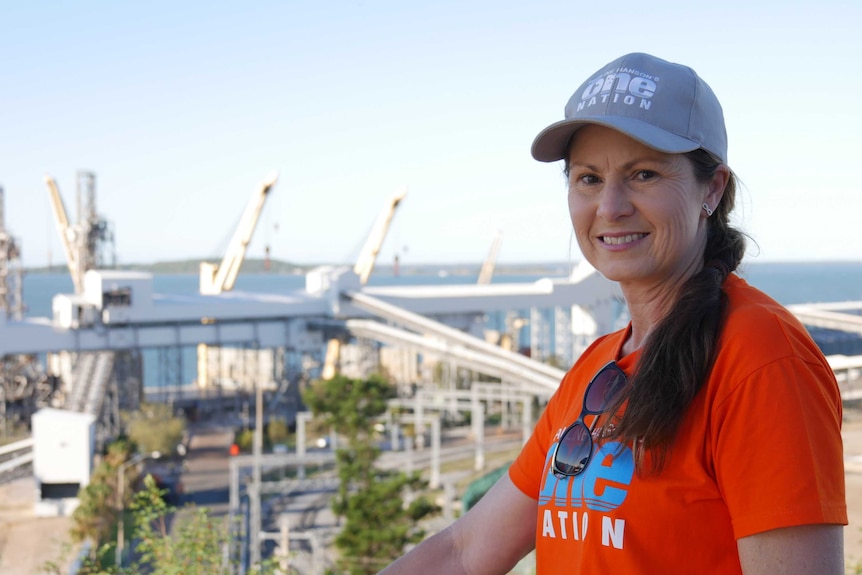 A woman wearing a hat stands in front of a power station in Central Queensland