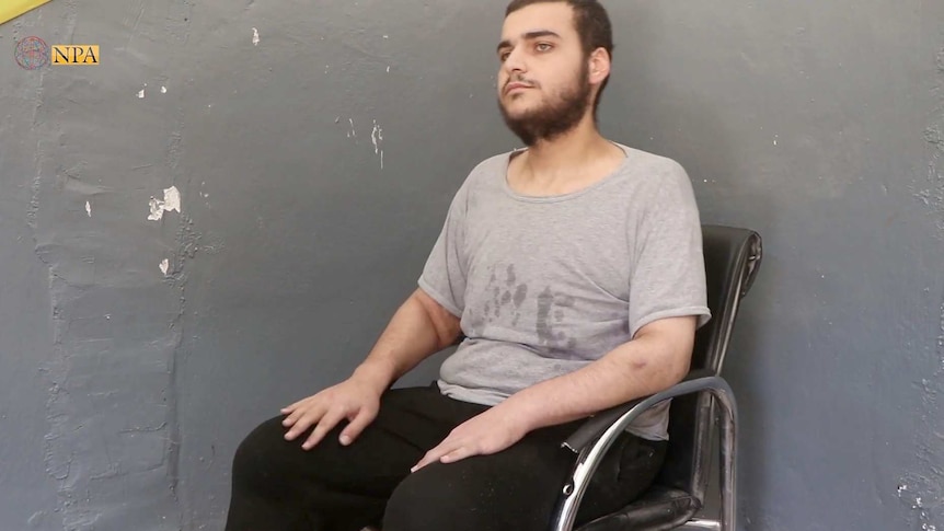 Hamza Elbaf sits in a black chair against a grey wall.