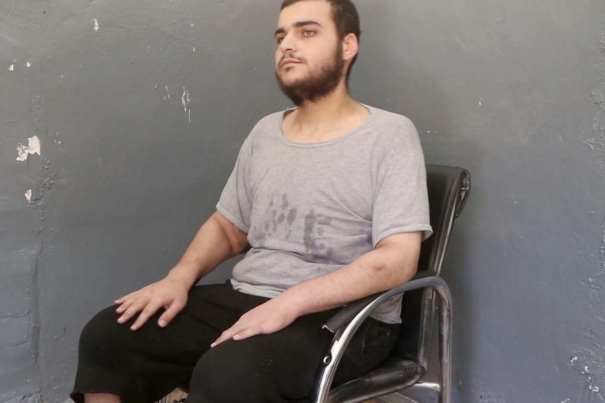 Hamza Elbaf sits in a black chair against a grey wall.