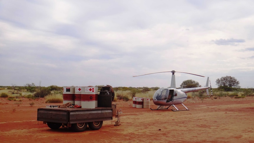 A helicopter sits on the red dirt.