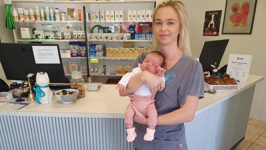 woman with blonde hair holds tiny baby with pink pants stand in vet surgery