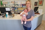 woman with blonde hair holds tiny baby with pink pants stand in vet surgery