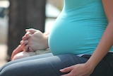 A pregnant woman's belly as she holds hands with someone