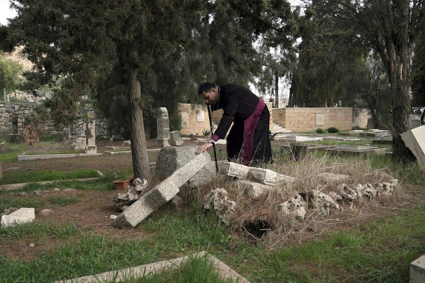 A Palestinian Anglican bishop, touches a damaged grave where vandals desecrated more than 30 graves.