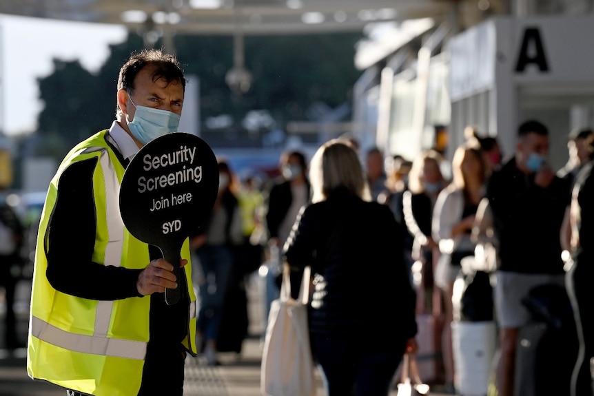 A man in high vis holds a sign alerting of security screening