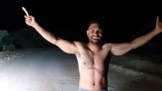 A shirtless man smiles with arms outstretched.