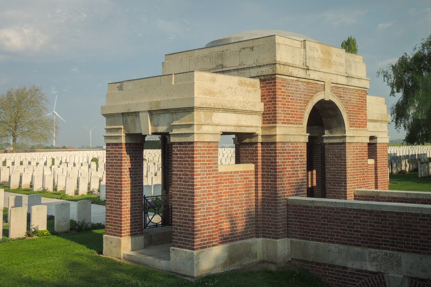 An arch and domed brick entrance to a war cemetery in front of memorial headstones.