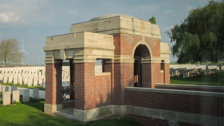 An arch and domed brick entrance to a war cemetery in front of memorial headstones.