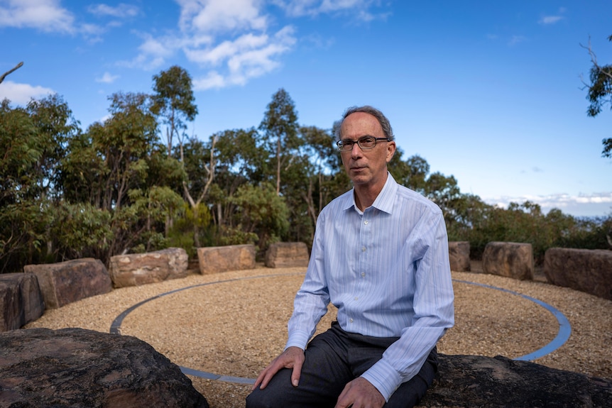 David Karoly sits on a rock and looks at the camera with a serious expression.