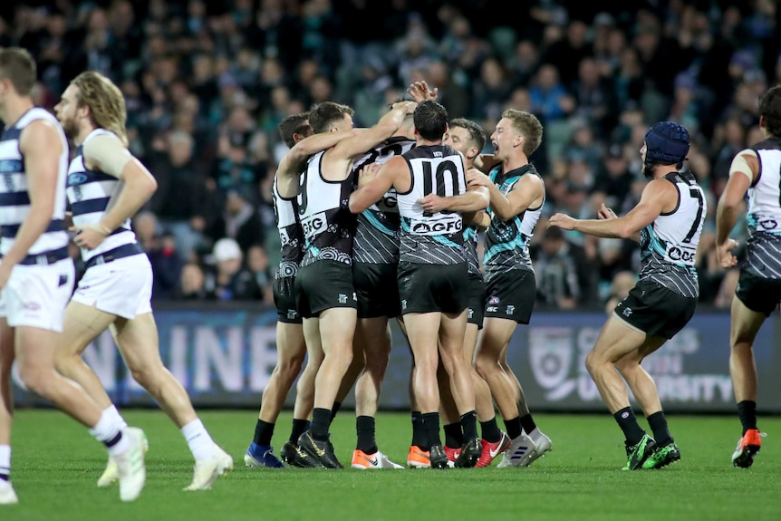 A group of Port Adelaide players huddle around an obscured Dixon. Geelong players are disappointed in the foreground.