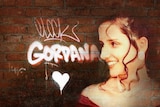 A wall with Gordana spray painted on it next to a photo of Gordana with brown curly hair  