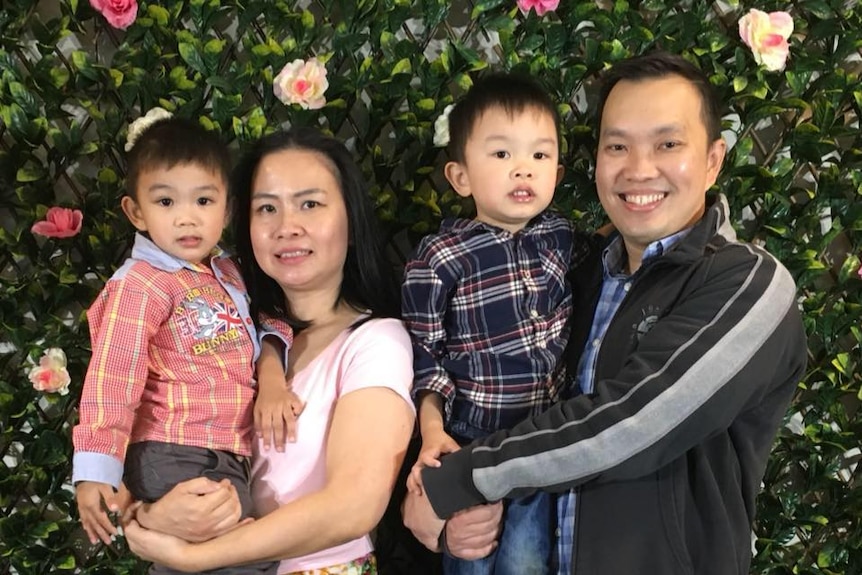 A woman holding a child stands next to her husband, holding another child. All are smiling at the camera.