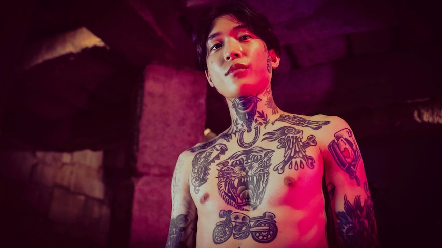 A young shirtless Korean man with his chest, neck and arms covered in tattoos