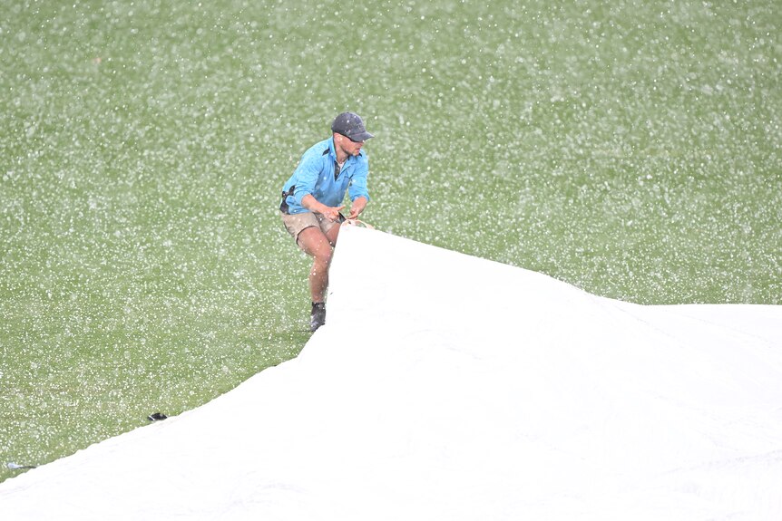 A groundskeeper pulls a cover over the pitch as hail falls around him