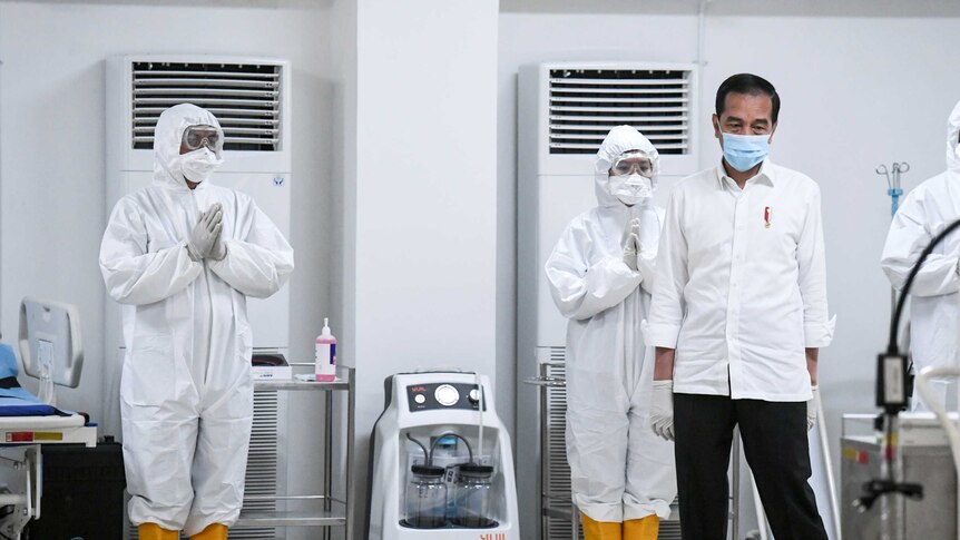 Indonesia's President Joko Widodo stands alongside two medical workers in hazmat suits.