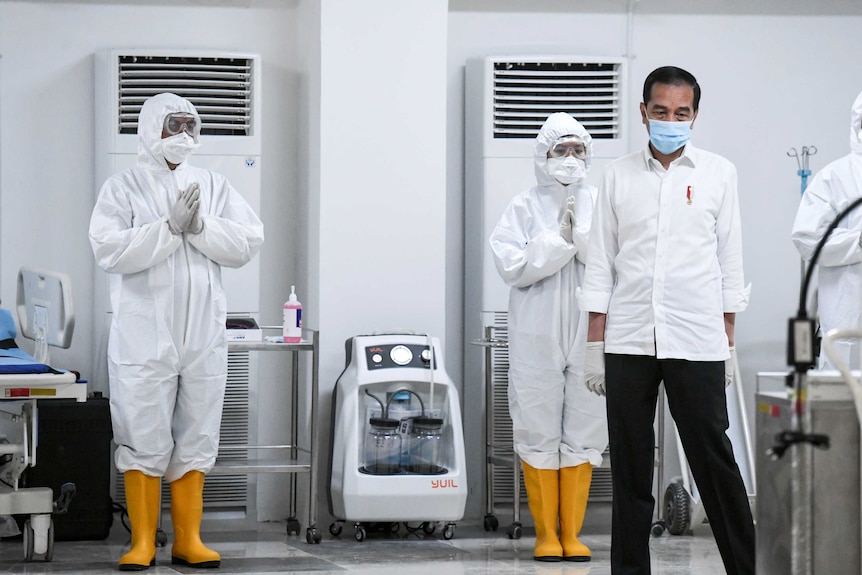 Indonesia's President Joko Widodo stands alongside two medical workers in hazmat suits.