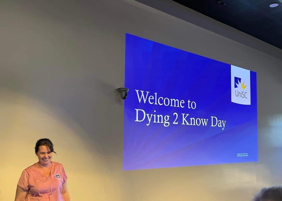 Woman standing infront of a powerpoint slide that reads Welcome to Dying 2 Know Day. 