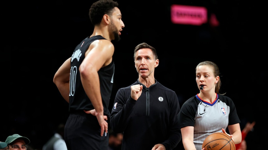 Brooklyn Nets coach Steve Nash speaks to Ben Simmons as an NBA referee looks on with the ball in hand.