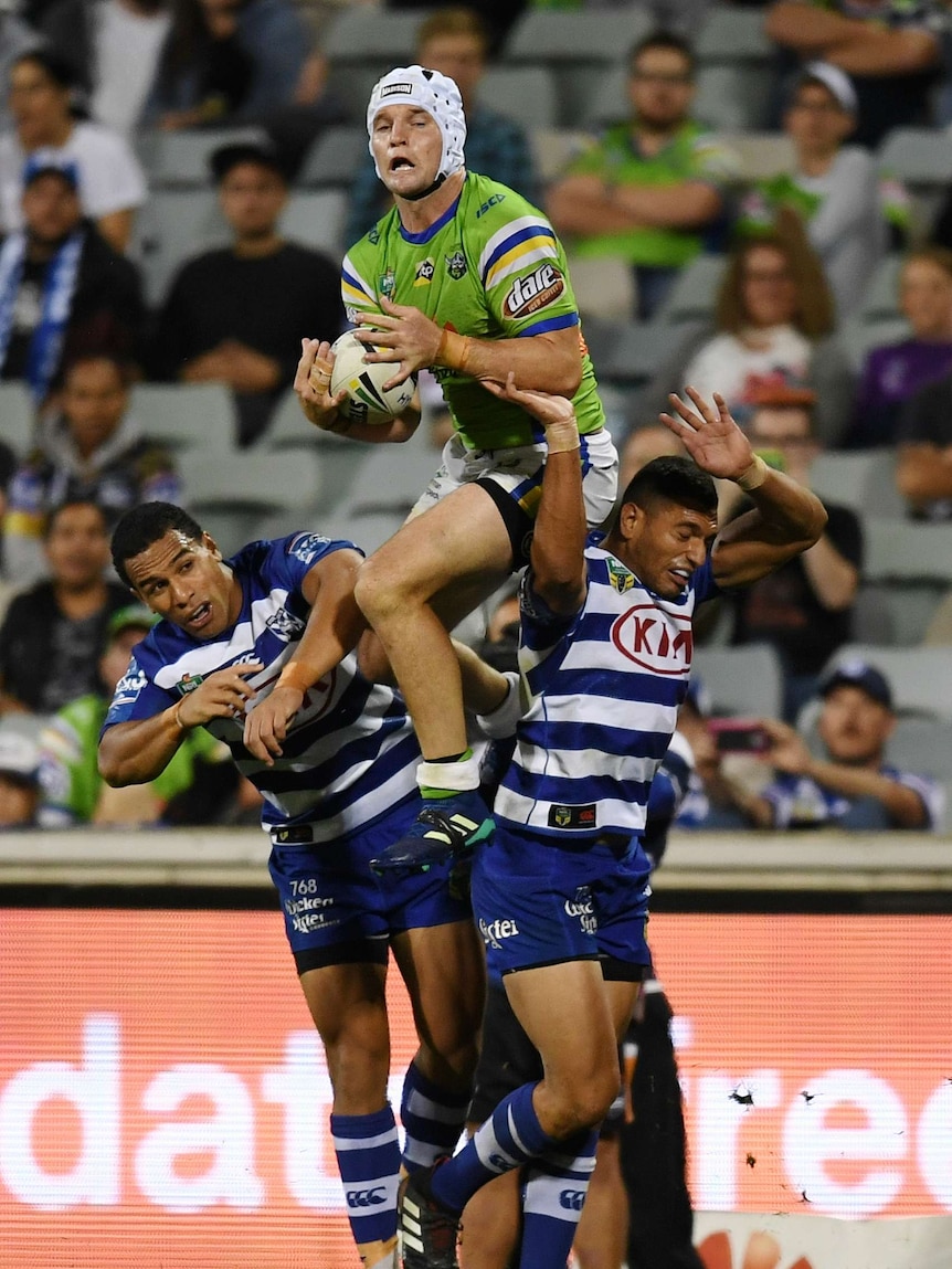 Raiders captain Jarrod Croker leaps above two Bulldogs players to catch a kick