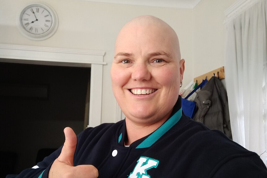 A woman who has undergone cancer treatment gives a thumbs up and smiles.