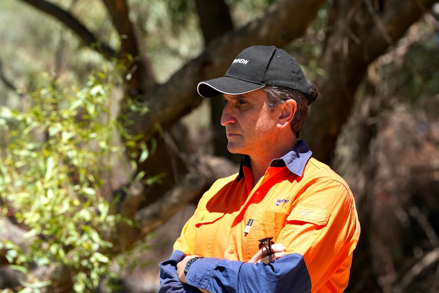 A man wearing a black hat and orange shirt staring in the distance. 