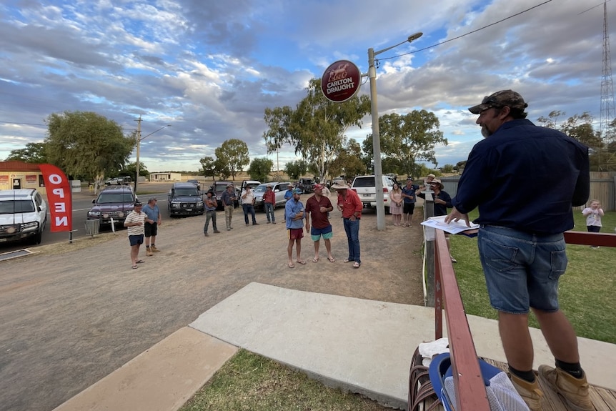 a man stands on a step, talking to locals at a pub 