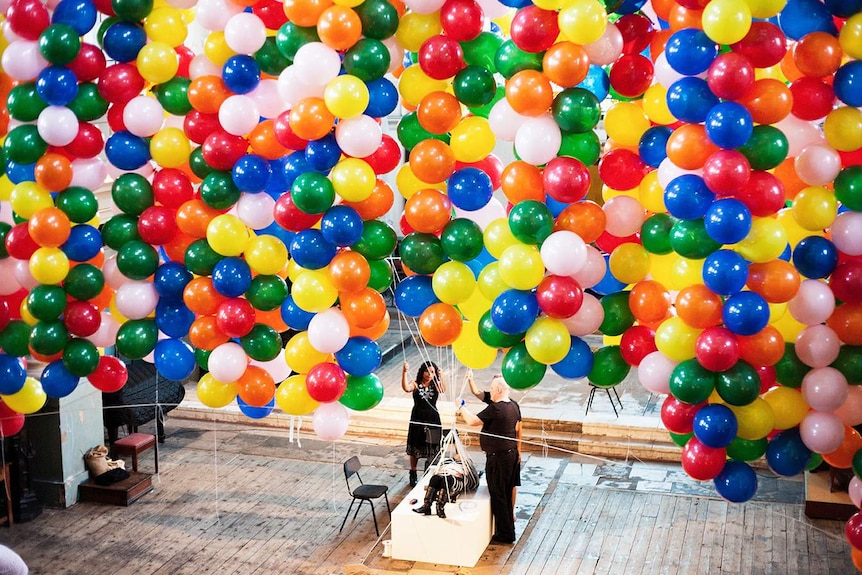 Colour photography of live artist Noëmi Lakmaier being bound by ropes to 20,000 balloons inside a church.