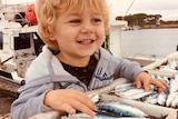 A toddler grins next to a big catch of sardines. The photo is close on his face
