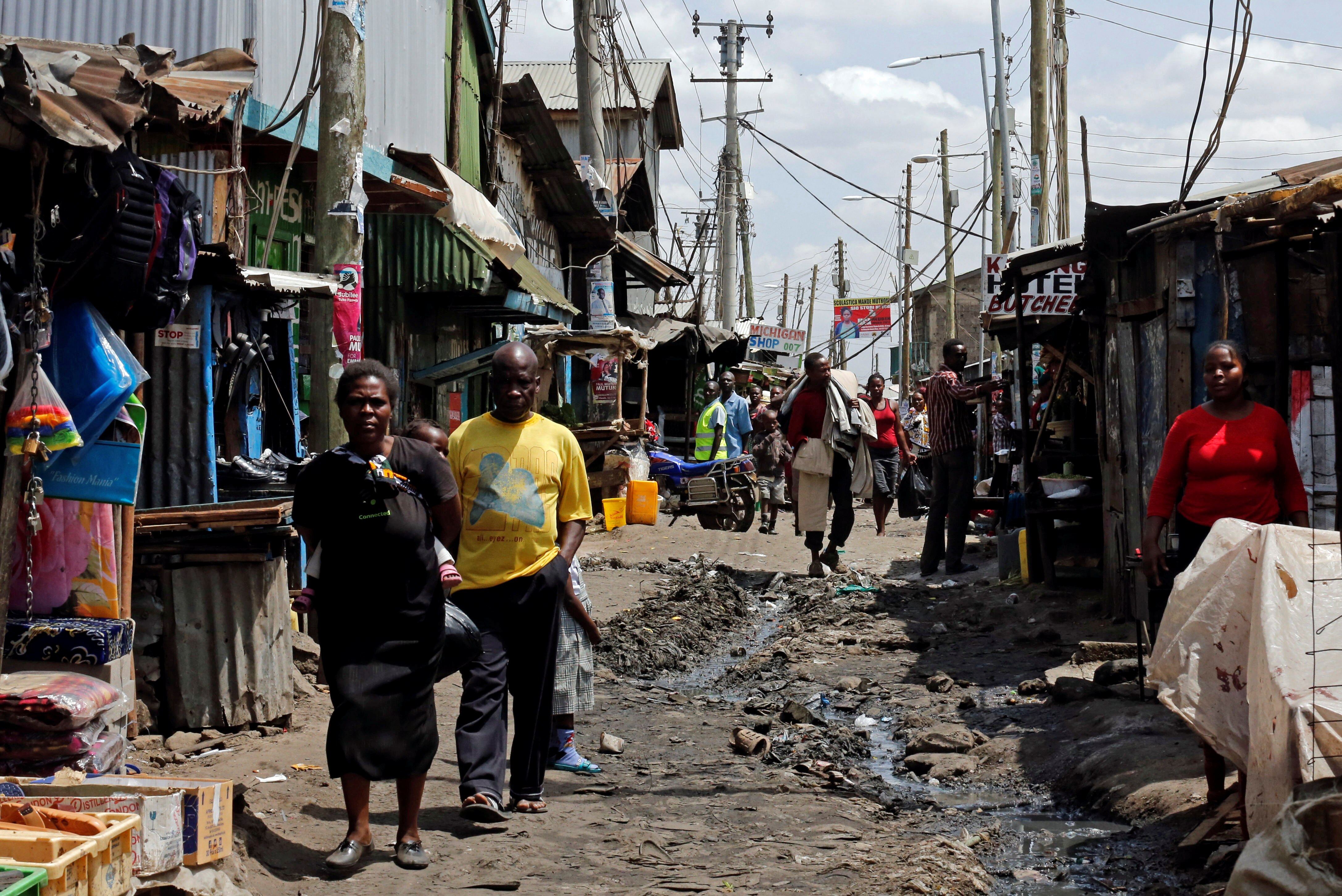 People walk along a dirt road among shanties 