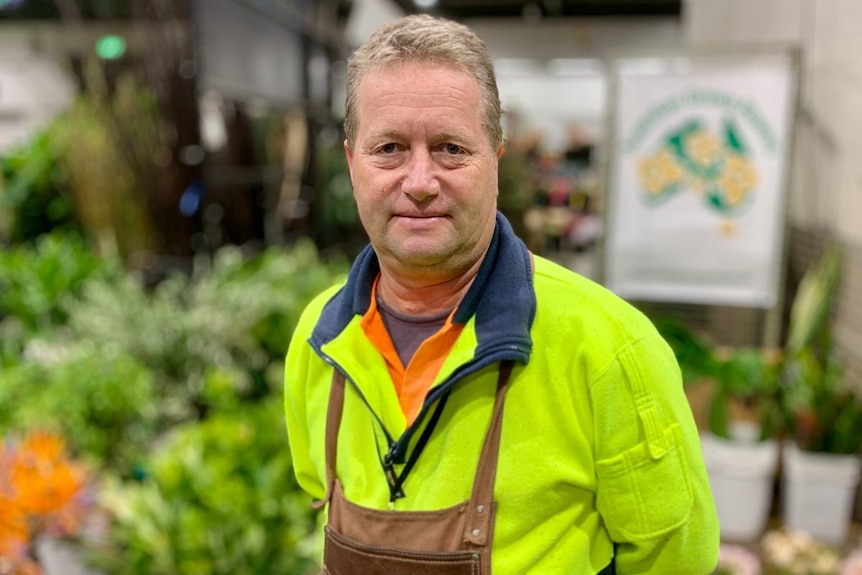 A man stands in a flower market wearing high vis and an apron.