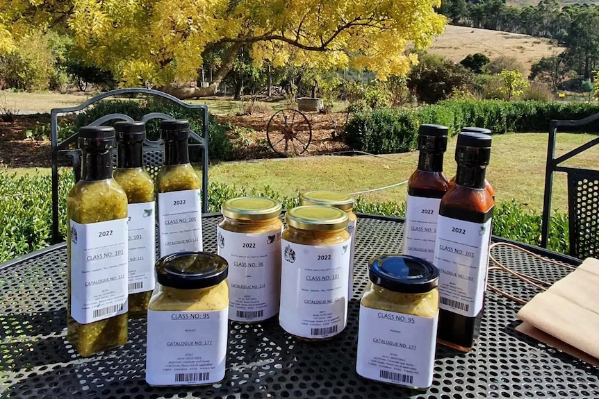 Jars of relish and pickles and sauce on a table outside in the country.