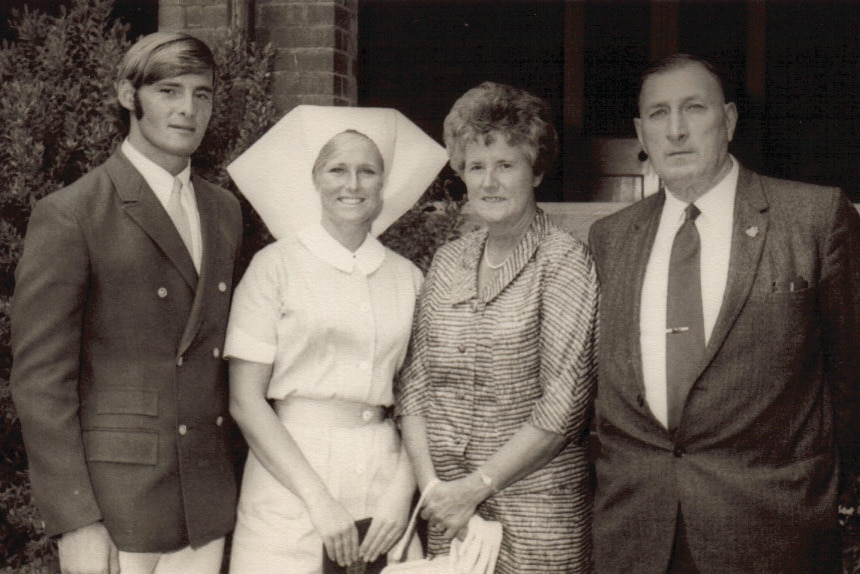 1960s photo in black and white of woman in white nursing uniform standing beside young man, older woman and older man in suits