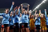 A women's soccer team wearing sky blue holds up a trophy after winning a major tournament