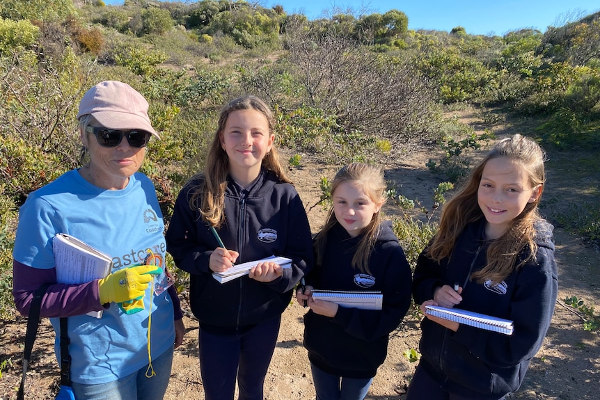 Woman with gloves and notebook, hat and sunglasses with three girls holding notebooks looking at the camera.