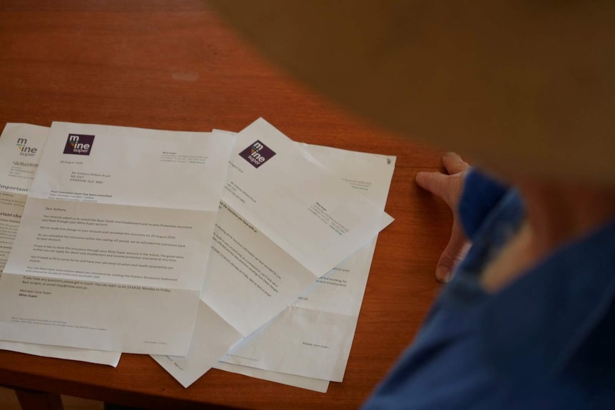 A photo of some paperwork on a table, with a hat and a hand visible in the frame.