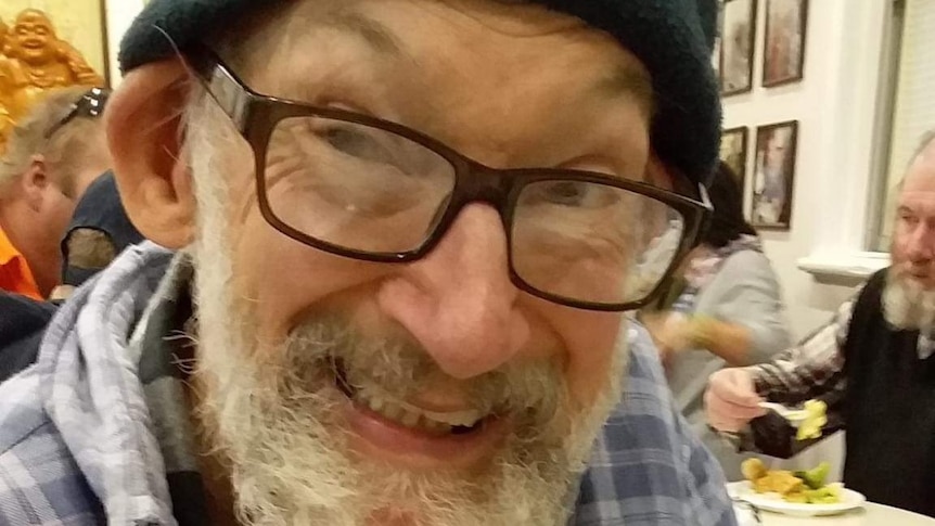 An older man in a beanie and spectacles, smiling warmly.