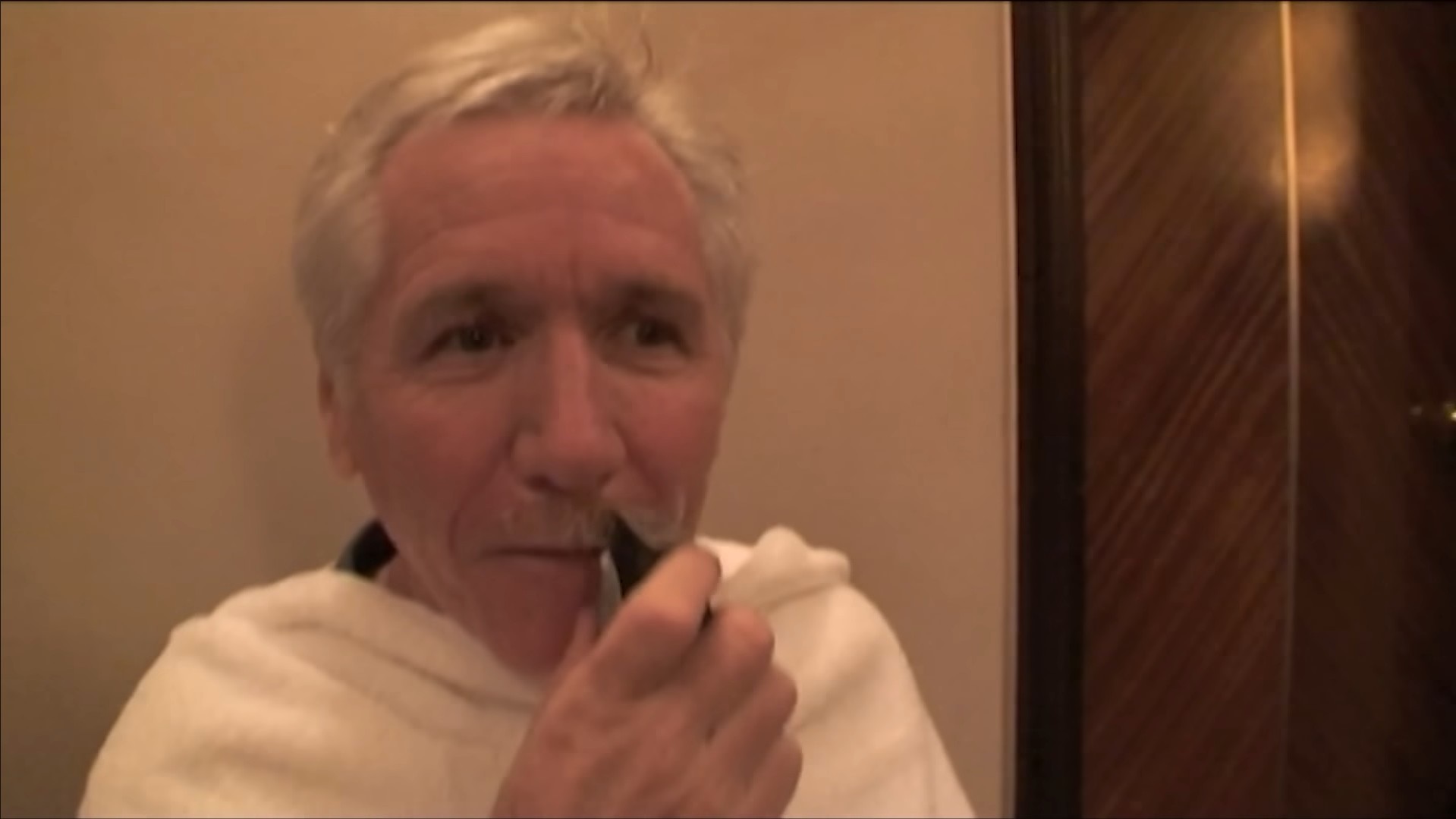 A man with grey hair has his grey moustache shaved with an electric razor