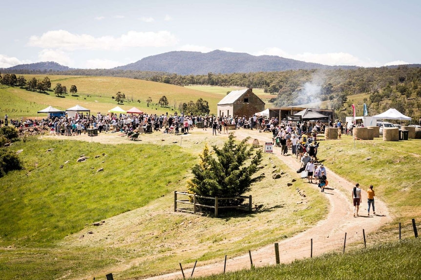 a crowd of people in a field with historic farm shed in background