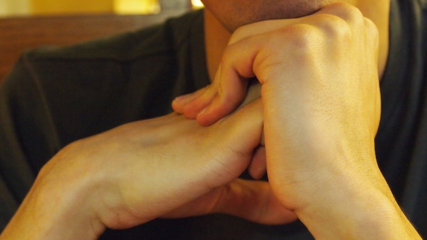 A close-up of a man cracking his knuckles in front of his face. 