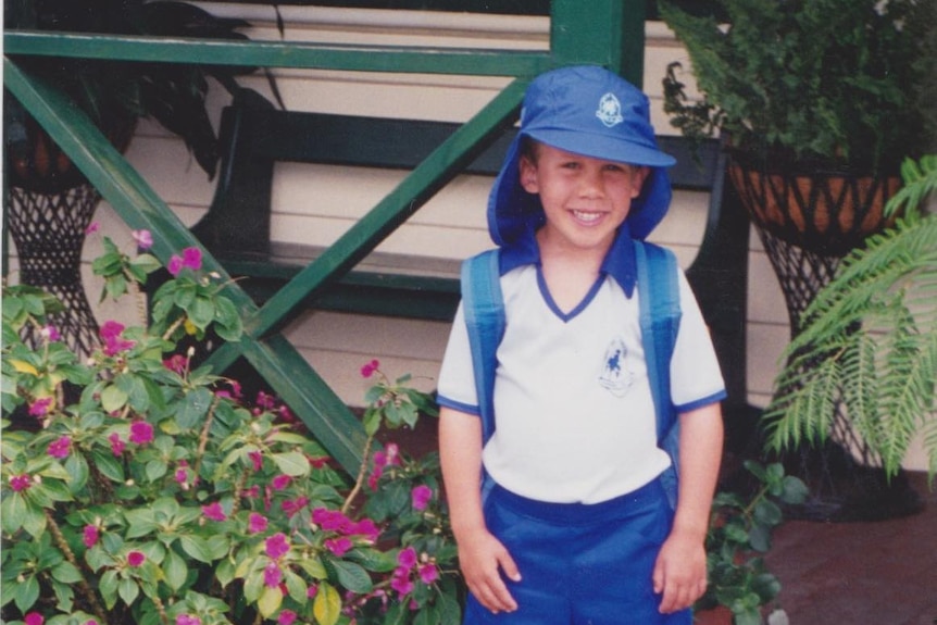  A young boy wearing his school uniform and school bag outside a home.